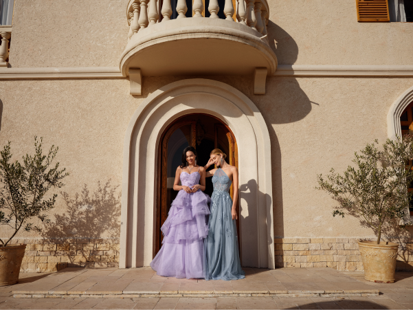 Two models in long prom dresses, one in lilac and the other in dusty blue.